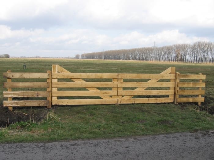 Landhekken van hout met dubbele draaipoorten en robuuste erfafscheiding in een open agrarisch landschap