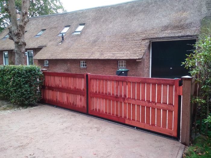 Rode houten schuifpoort op maat in Veghel bij landelijke woning met rieten dak
