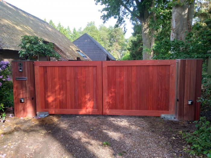 Dubbele houten poort van padouk met gesloten verticale planken bij een landelijke woning.