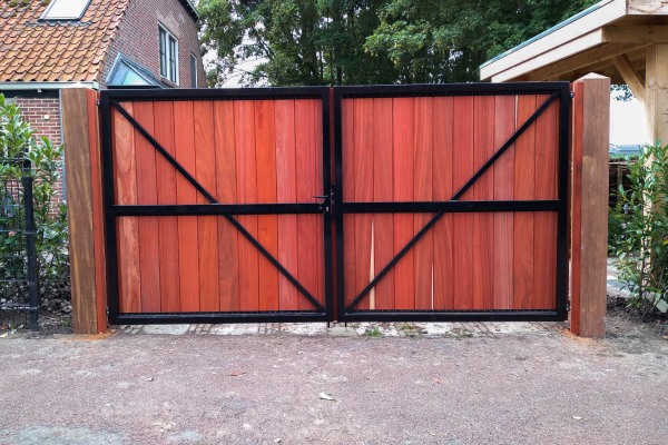 Dubbele padouk houten poort met zwarte metalen omlijsting en verticale planken.