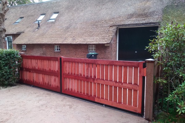 Dubbele padouk poort met verticale houten delen bij een landelijke boerderij.