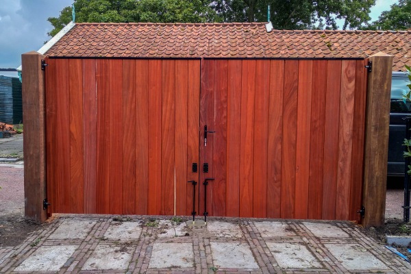 Gesloten dubbele poort van padouk met verticale houten planken en zwart hang- en sluitwerk.
